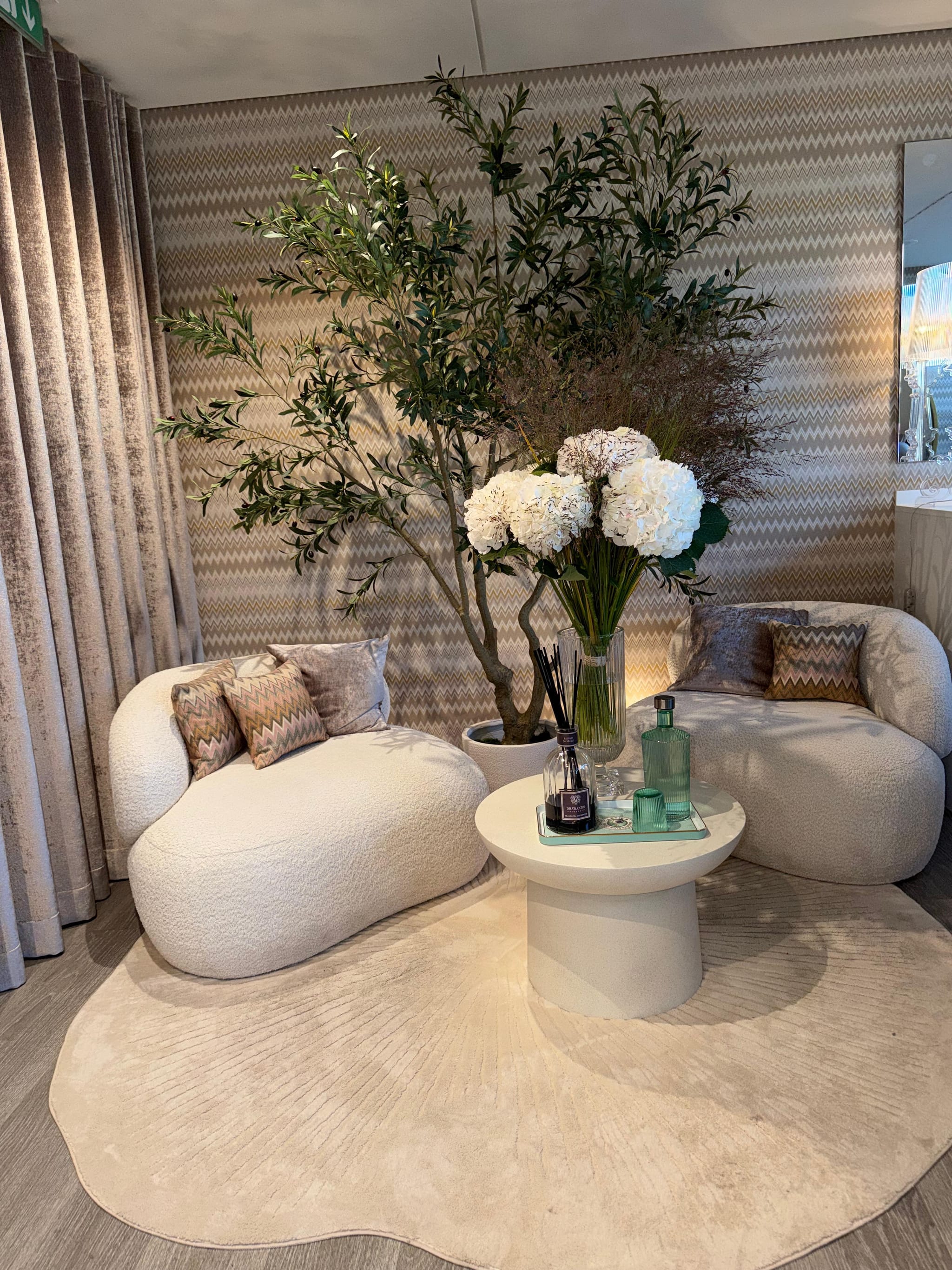 Wartelounge mit geschwungenem Sofa, Olivenbaum und Hortensien